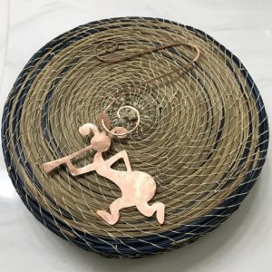 Copper Kokopelli Ornament with Hanger on a blue and tan basket background. This image has more light on the ornament.